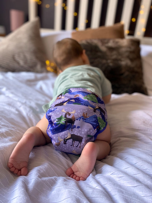 Small child wearing a moose print reusable cloth nappy crawling away from the camera.