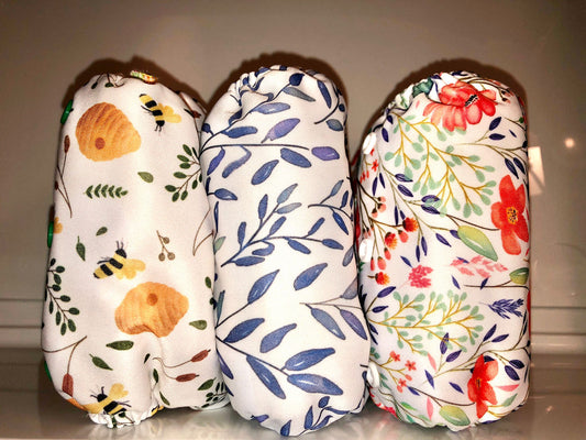 Image of three cloth nappies that come in this set. One with a bee print, one with a blue leaf print and one with a pink and blue flower print. 