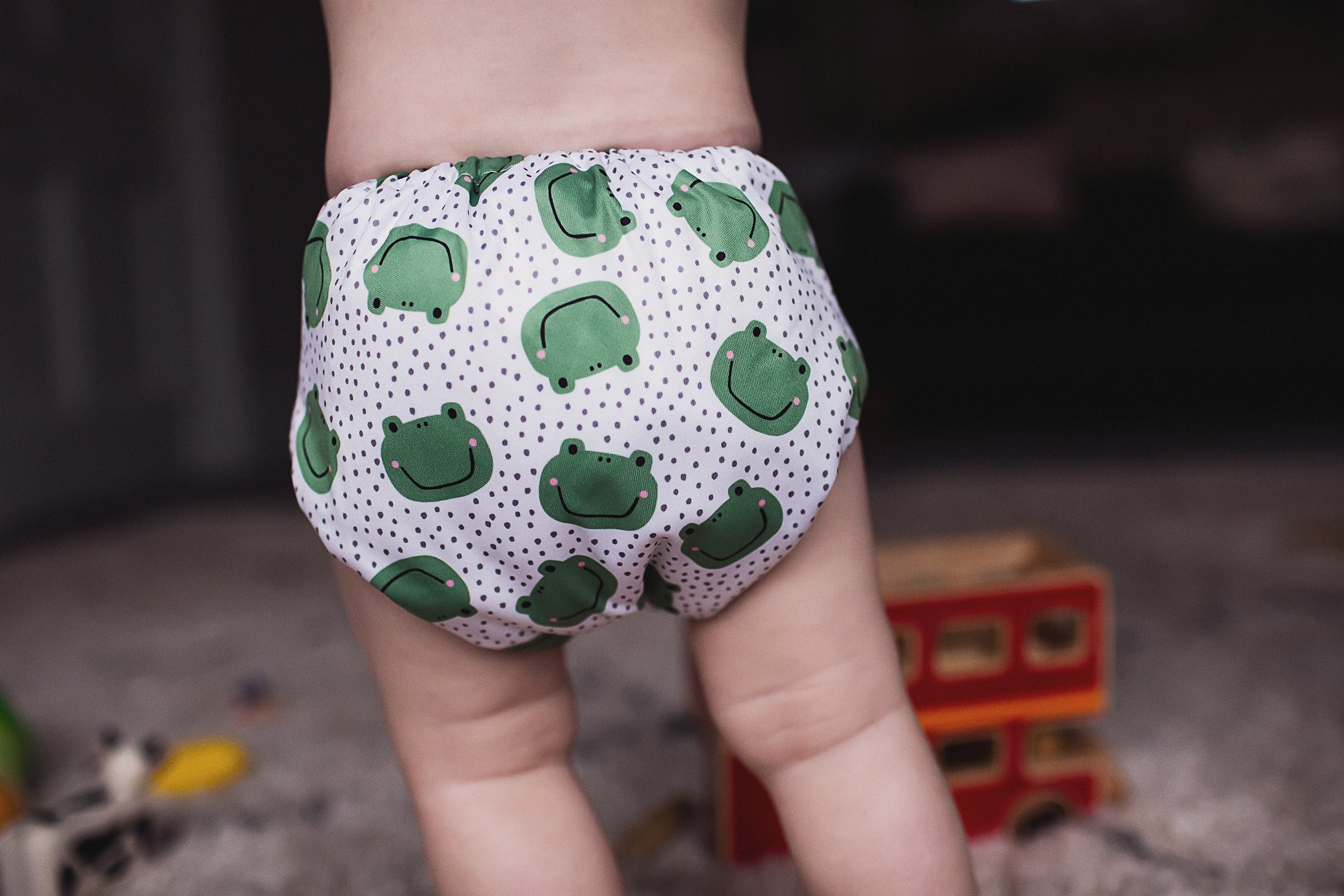 A small child wearing a frog print reusable cloth nappy walking away from the camera. 