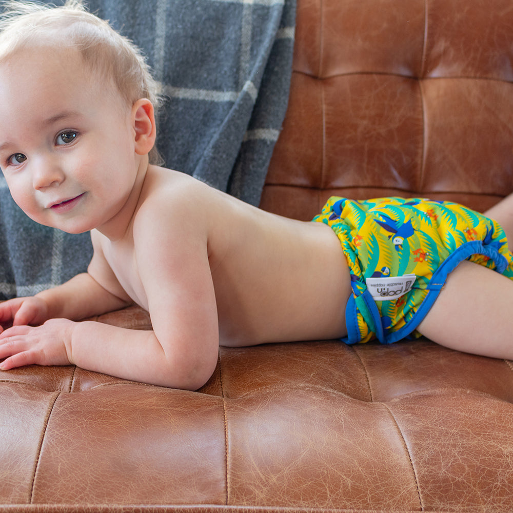 Small child lying on their front wearing a reusable cloth nappy with a parrot print.