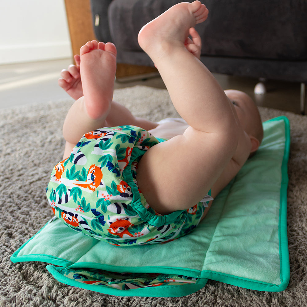Small child lying on their back wearing a reusable cloth nappy with a red panda print.