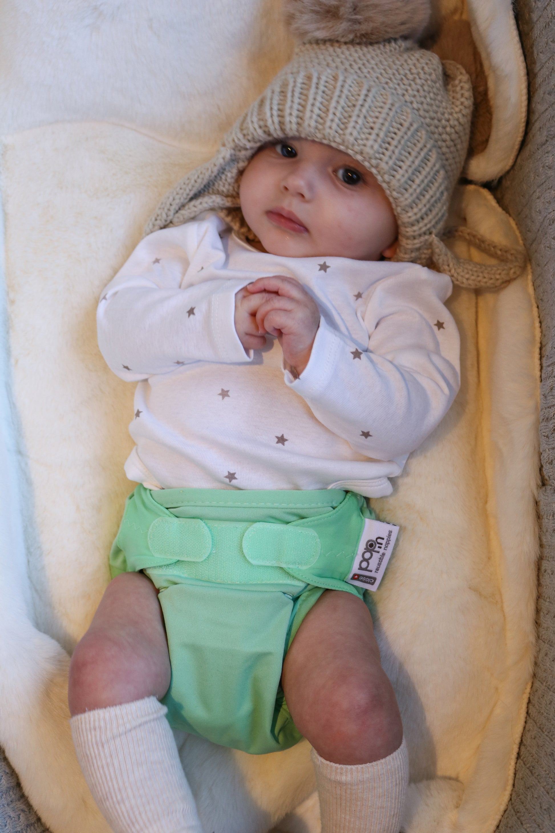 Image shows a baby wearing a green reusable cloth nappy with velcro fastening. 