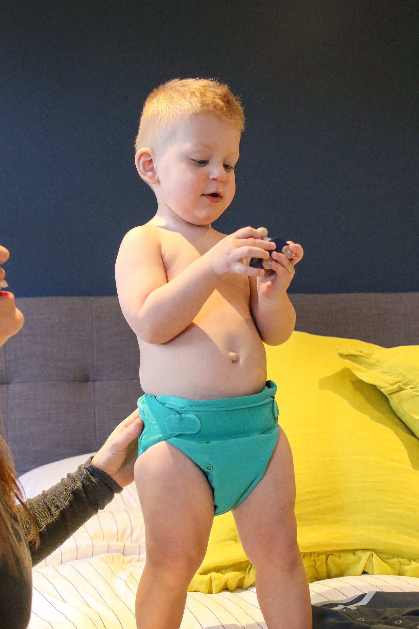 Image showing a small child wearing a reusable cloth nappy in a green colour with velcro fastening.
