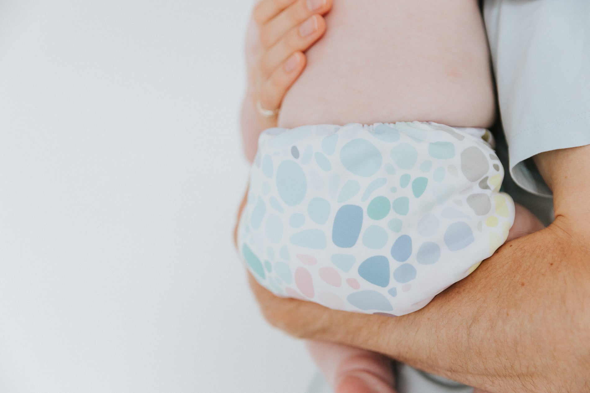 A small child wearing a reusable cloth nappy with a pastel pebble pattern. The child is being held by an adult. 