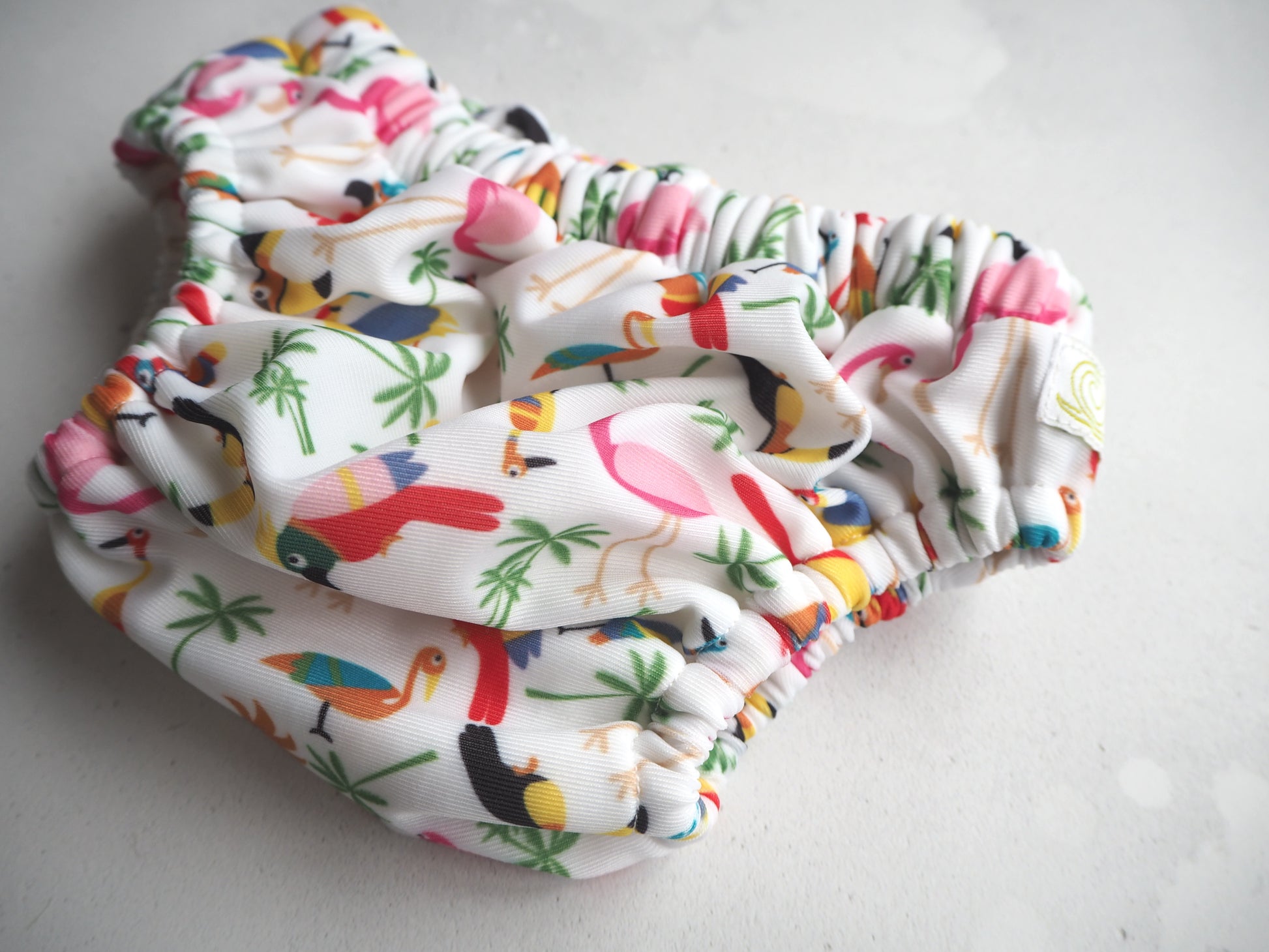 Image of a reusable swim nappy. Pattern is with brightly coloured birds in a tropical rio theme. 