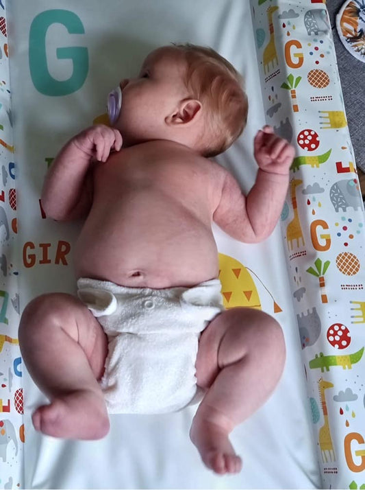 Image of a baby lying on a changing mat wearing the size 1 fitted nappy